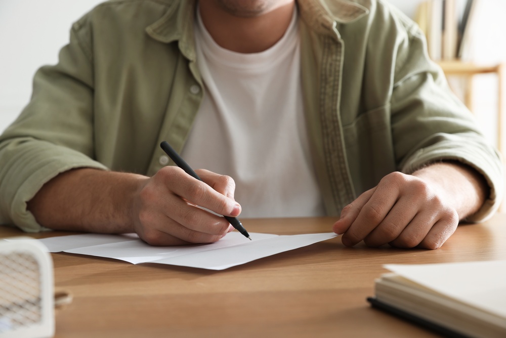 man,writing,letter,at,wooden,table,indoors,,closeup